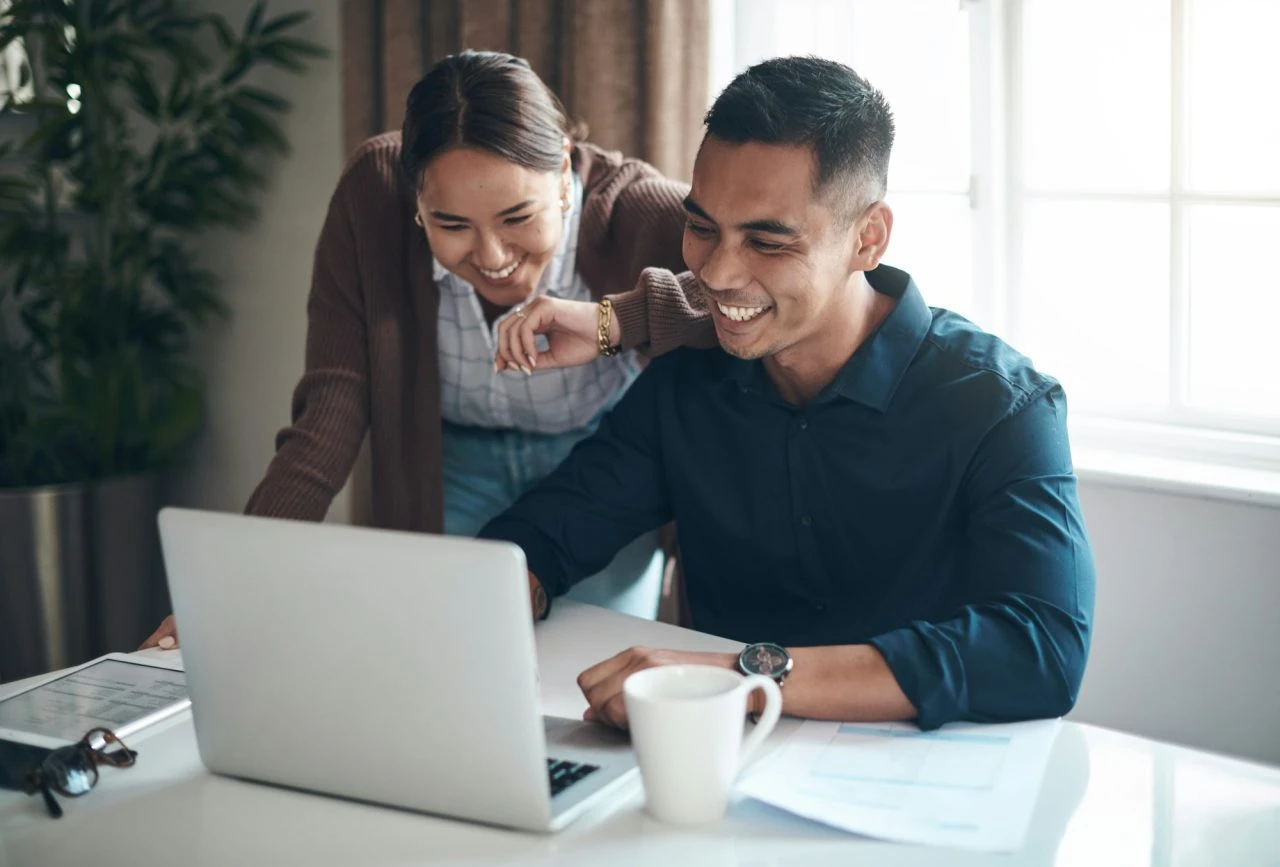 Dos empresarios sonriendo frente a una laptop, representando la tranquilidad de una MYPE al contar con un planeamiento tributario proactivo que evita multas de SUNAT.